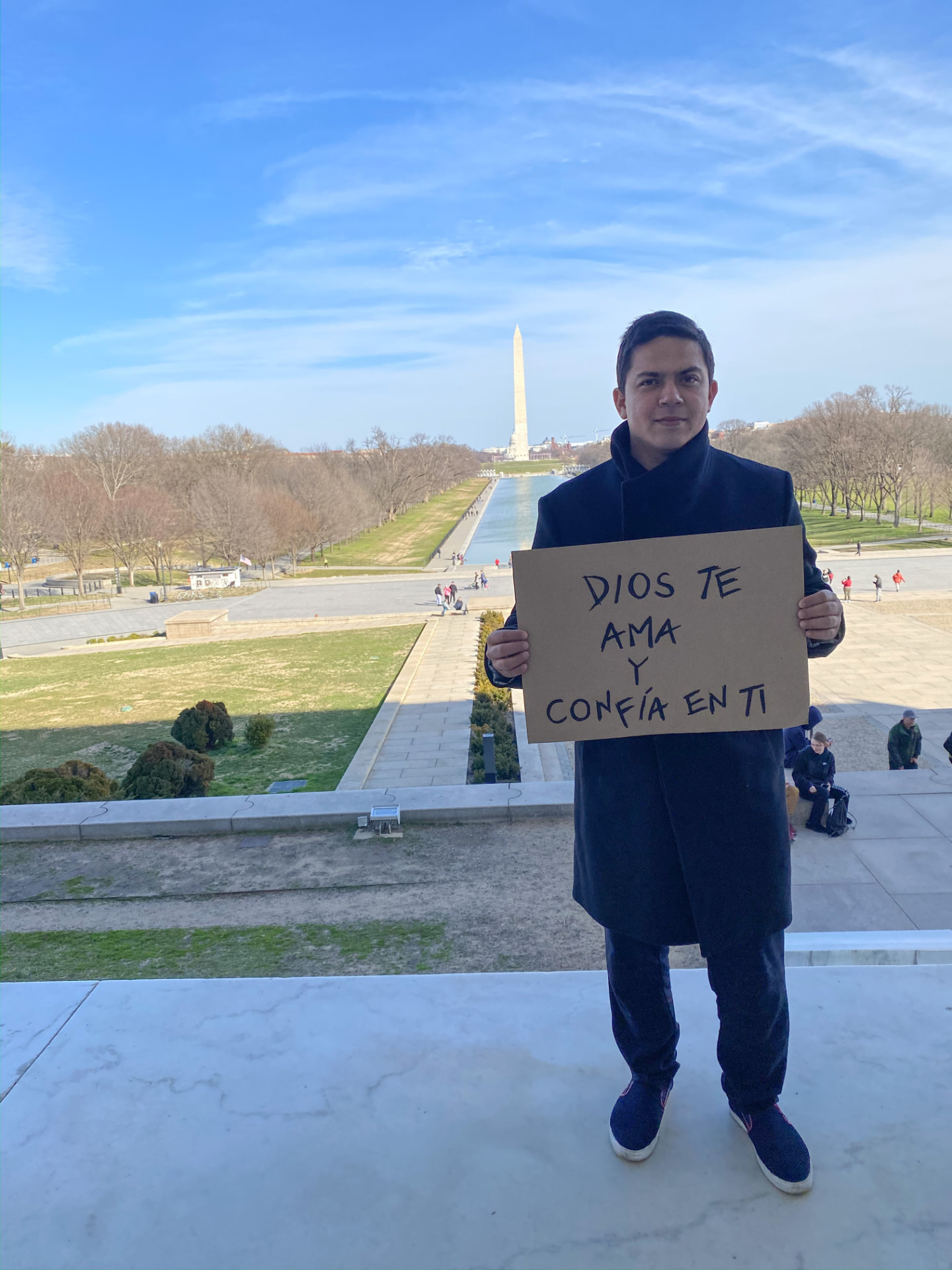 Frank Zapata sosteniendo un cartel que dice 'Dios te ama y confía en ti' frente al Monumento a Washington