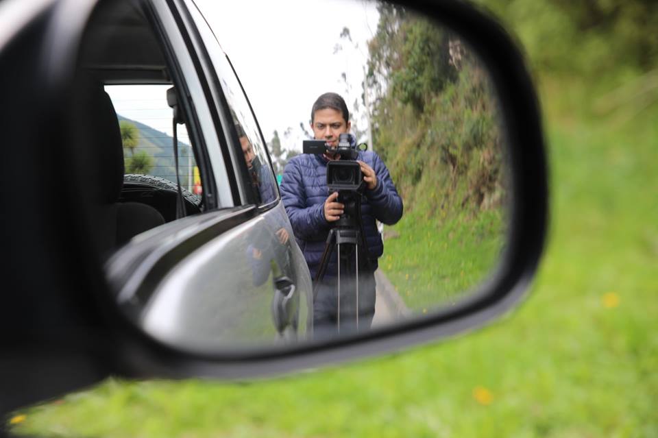 Frank Zapata filmando con cámara profesional reflejada en el espejo retrovisor de un carro